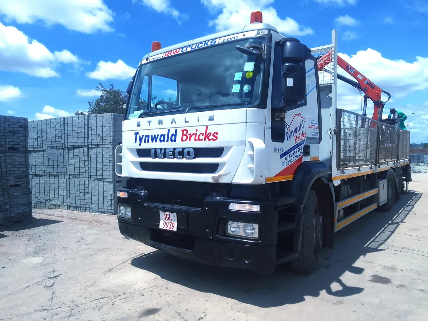 A Tynwald Bricks truck fitted with a grabber crane, alongside stacked blocks at the yard